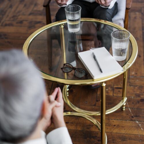 pexels-cottonbro-studio-4098369 Bild på ett soffbord med glas och block på sig. Två personer sitter runt